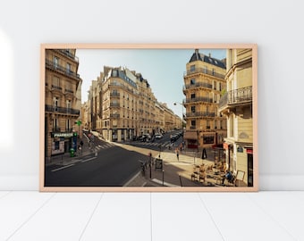 May include: A street scene in Paris, France, with a view of several buildings, including a pharmacy. The street is lined with trees and there are people walking on the sidewalk. The buildings are all made of stone and have a traditional French architecture. The street is empty of cars and there is a cafe on the right side of the street.