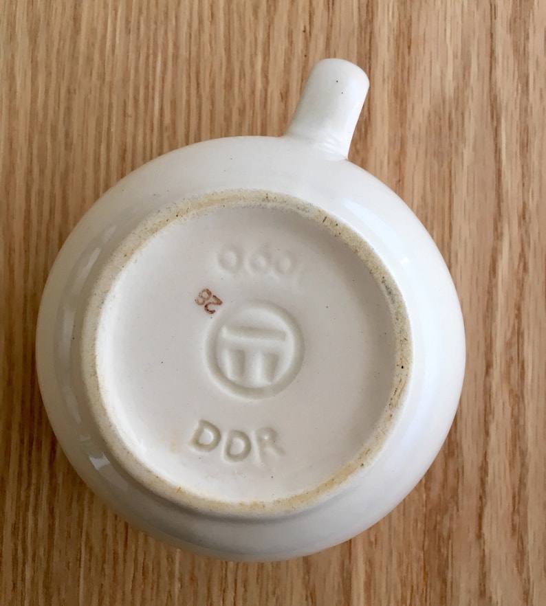 Pu&ograve; includere: Tazza in ceramica bianca con manico. Il fondo della tazza ha un timbro marrone con il testo "DDR" e un simbolo con il numero "963" e "32".