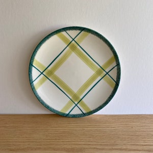 May include: A white ceramic plate with a green and yellow plaid design. The plate has a slightly raised rim.