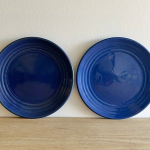 Peut inclure: Deux assiettes en céramique bleues avec un bord surélevé et un motif de cercles concentriques. Les assiettes sont sur une surface en bois.