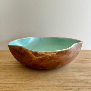 May include: A light brown ceramic bowl with a light blue glaze on the inside. The bowl has a slightly irregular shape and a rustic look.