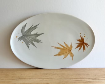 May include: White oval serving platter with a gray and brown leaf design. The leaves are stylized and have a delicate, almost watercolor-like appearance.