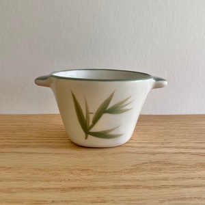 May include: A small white ceramic creamer with green leaf designs and two handles.