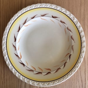 May include: A white ceramic soup bowl with a yellow rim and brown leaf design. The bowl has a rope-like edge.