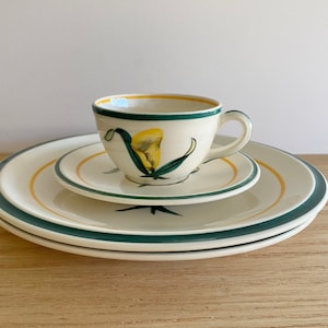 K&ouml;nnte beinhalten: Ein wei&szlig;es Porzellan-Teetassen-Set mit einem gr&uuml;nen und gelben Blumendesign. Die Tasse hat einen Henkel und die Untertasse einen gr&uuml;nen Rand.