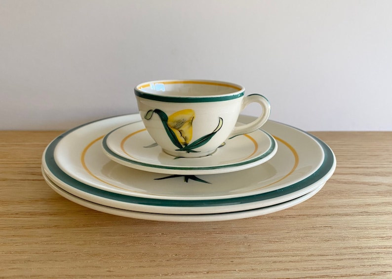 K&ouml;nnte beinhalten: Ein wei&szlig;es Porzellan-Teetassen-Set mit einem gr&uuml;nen und gelben Blumendesign. Die Tasse hat einen Henkel und die Untertasse einen gr&uuml;nen Rand.