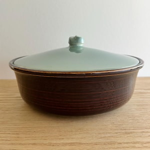 Könnte beinhalten: Eine braune Keramik-Servierplatte mit einem hellgrünen Deckel. Die Platte hat ein strukturiertes, geripptes Muster und eine leicht abgerundete Form.