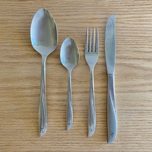 Könnte beinhalten: Ein Set aus drei silberfarbenen Besteckteilen, bestehend aus einer Gabel, einem Messer und einem Löffel. Die Griffe jedes Teils haben ein dekoratives Sternmuster.