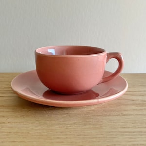Peut inclure: Un ensemble tasse et soucoupe rose poudré. La tasse a une forme arrondie avec une anse incurvée, posée sur une soucoupe assortie. L'ensemble est en céramique et posé sur une surface en bois. Un design simple et élégant pour servir le thé ou le café.