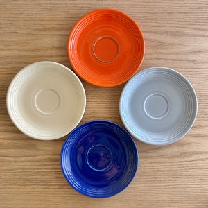 Puede incluir: Cuatro platillos de cerámica en diferentes colores: naranja, blanco, azul claro y azul oscuro. Cada platillo tiene un centro ligeramente elevado.