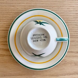 K&ouml;nnte beinhalten: Eine wei&szlig;e Teetasse und Untertasse mit gr&uuml;nem und gelbem Rand. Die Teetasse hat ein Blumenmuster und den Text "FREDERIK LUNNING, INC. NEW YORK" auf der Unterseite.