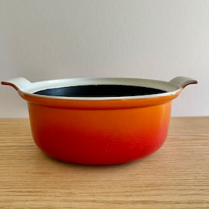 Pode incluir: Uma panela de ferro fundido esmaltada laranja e branca com duas alças.