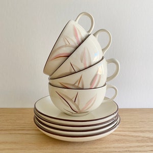 May include: A stack of four white ceramic teacups with a brown and pink floral design. The cups are stacked on top of four matching saucers.