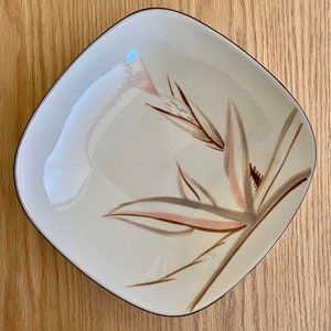 May include: A square, off-white ceramic dish with a brown rim. The dish features a stylised floral design in shades of brown and pink.