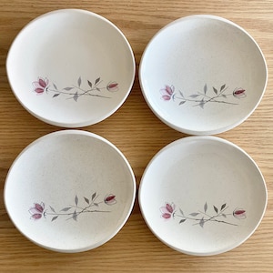 Op de afbeelding: Set van vier witte keramische dinerborden met een gespikkelde afwerking. Elk bord heeft een delicaat bloemenmotief met roze bloemen en grijze stelen.