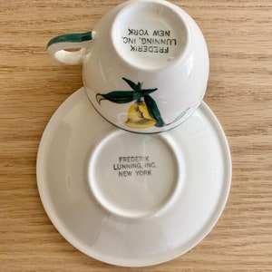K&ouml;nnte beinhalten: Eine wei&szlig;e Teetasse und Untertasse mit gr&uuml;nem Rand und einem gelben und gr&uuml;nen Blumendesign. Auf der Unterseite der Untertasse steht "FREDERIK LUNNING, INC. NEW YORK".