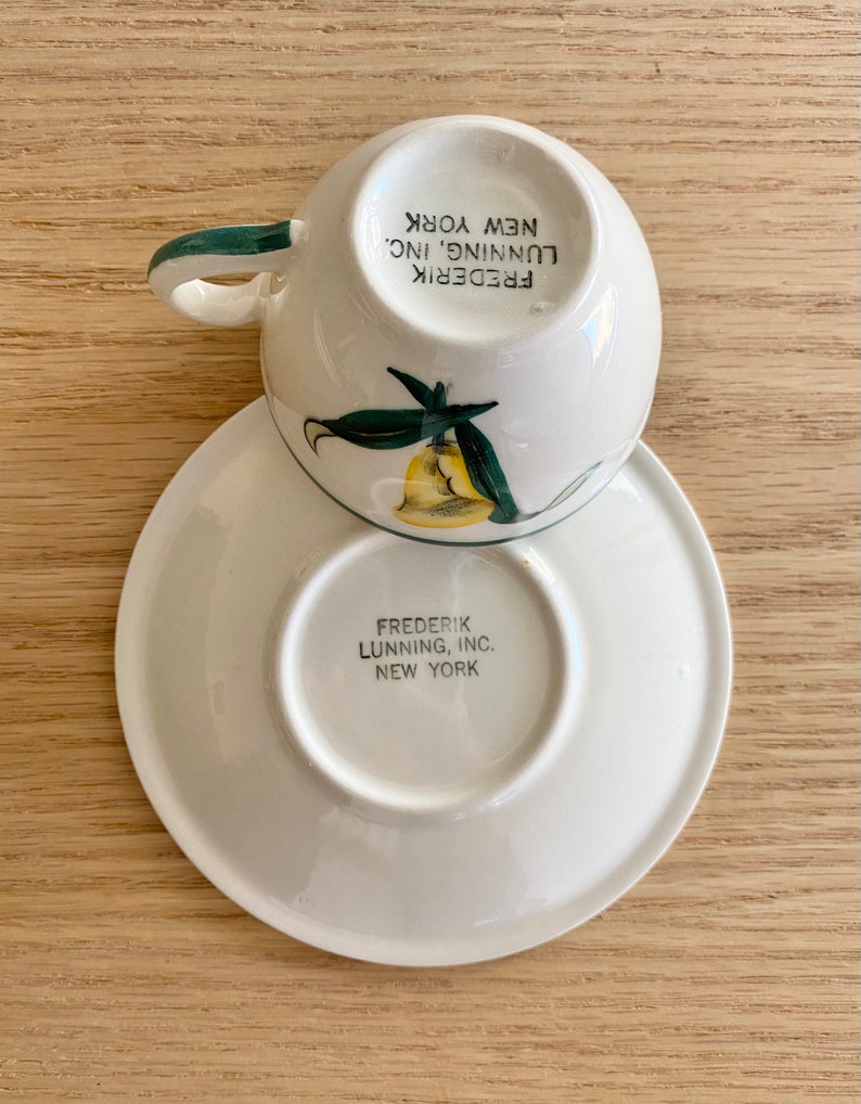 K&ouml;nnte beinhalten: Eine wei&szlig;e Teetasse und Untertasse mit gr&uuml;nem Rand und einem gelben und gr&uuml;nen Blumendesign. Auf der Unterseite der Untertasse steht "FREDERIK LUNNING, INC. NEW YORK".