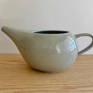 May include: A light grey ceramic creamer or gravy boat with a rounded body and a handle. The creamer has a smooth, glossy finish.
