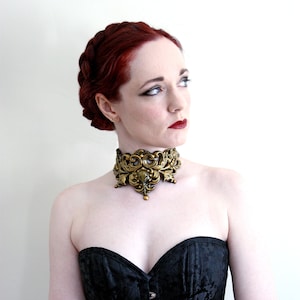 May include: A woman with red hair wearing a black strapless top and a gold ornate choker necklace.