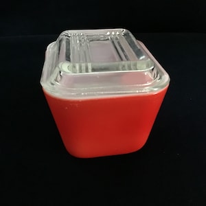 May include: A vintage red and clear glass rectangular dish with a clear glass lid. The dish has a vibrant red base and a clear, ridged lid. The design is simple and classic, suitable for kitchen or home decor.