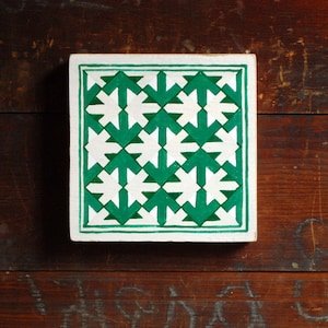 May include: A square tile with a geometric pattern of white stars on a green background. The tile is made of ceramic and has a white border.