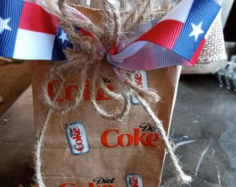Petit sac cadeau marron décoré d'un nœud rouge, blanc et bleu, contenant une boisson gazeuse. Parfait pour Noël, un anniversaire, un mariage, une récompense pour un professeur ou toute autre occasion.