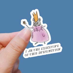 May include: A sticker featuring a cartoon rat wearing a pink dress and a gold crown, holding a star-shaped wand. The text "I AM THE EXECUTIVE OF THIS DYSFUNCTION" is below the rat. The sticker is held against a blue background.