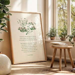 Könnte beinhalten: Ein gerahmter Kunstdruck mit einer Illustration von Rehen und einem Gedicht von Laura Gilpin. Das Kunstwerk befindet sich in einem hellen Holzrahmen, der an einer Wand lehnt. Die Szene umfasst ein Fenster mit Pflanzen und einen kleinen Holztisch.