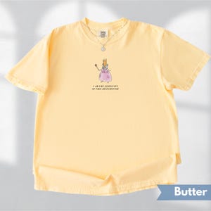 K&ouml;nnte beinhalten: Hellgelbes T-Shirt mit einer Cartoon-Illustration einer Maus als Prinzessin, die einen Zauberstab h&auml;lt. Der Text "I AM THE EXECUTIVE OF THIS DYSFUNCTION" steht darunter. Eine silberne Halskette ist sichtbar.