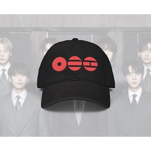 May include: Black baseball cap with a red graphic design. The design consists of three red shapes: a circle, a horizontal oval, and a rectangle with a horizontal line. The cap is made of a dark fabric.
