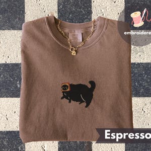Puede incluir: Sudadera color espresso con un gato negro bordado con tostadas. Un collar de cadena dorada con un colgante descansa sobre la camisa. La palabra "embroidered" est&aacute; encima de la camisa. La palabra "Espresso" est&aacute; debajo.