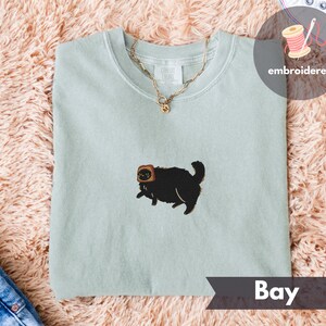Puede incluir: Sudadera de cuello redondo verde claro con un gato negro bordado con una rebanada de pan tostado en la cabeza. Una cadena dorada cuelga sobre la camisa. La palabra "Bay" est&aacute; impresa en una pancarta en la parte inferior.