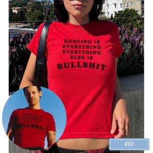 May include: A bright red short-sleeved t-shirt featuring the black text DANCING IS EVERYTHING EVERYTHING ELSE IS BULLSHIT printed on the front. The shirt has a crew neckline and a fitted silhouette, shown in both a main view and a circular inset.