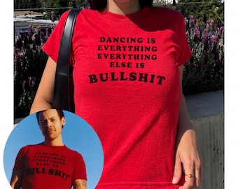 Op de afbeelding: Een felrood T-shirt met korte mouwen en de zwarte tekst DANCING IS EVERYTHING EVERYTHING ELSE IS BULLSHIT op de voorzijde. Het shirt heeft een ronde hals en een aansluitende pasvorm, getoond in zowel een hoofdafbeelding als een cirkelvormig inzetstuk.