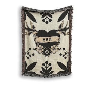 May include: A woven throw blanket with a black and white design featuring a heart with the word "MOM" on it, two birds, and floral accents.