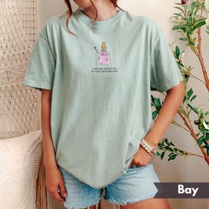 K&ouml;nnte beinhalten: Hellgr&uuml;nes T-Shirt mit einer Cartoon-Maus in einem rosa Kleid und Krone, die einen Zauberstab h&auml;lt. Der Text "I AM THE EXECUTIVE OF THIS DYSFUNCTION" ist darunter aufgedruckt. Das Shirt wird mit Jeansshorts getragen.