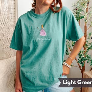 K&ouml;nnte beinhalten: Hellgr&uuml;nes T-Shirt mit einer Cartoon-Illustration einer Maus mit Krone und rosa Kleid, die einen Zauberstab h&auml;lt. Der Text auf dem Shirt lautet "I AM THE EXECUTIVE OF THIS DYSFUNCTION".