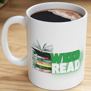 Pode incluir: Caneca de cerâmica branca com um design verde e branco que diz "Weed & Read" com uma pilha de livros coloridos e um livro aberto no topo. A caneca está cheia de café preto.