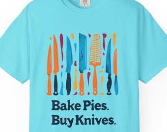 Puede incluir: Camiseta azul claro con un diseño colorido de cuchillos de varias formas. El texto "Bake Pies. Buy Knives." está impreso debajo. La camiseta está hecha de un material suave y es adecuada para el uso diario.