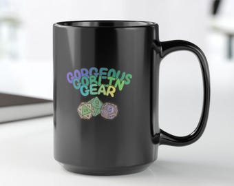 May include: A black ceramic mug with the text "Gorgeous Goblin Gear" in a colorful, gradient font. Below the text are three dice illustrations. The mug is on a white surface.