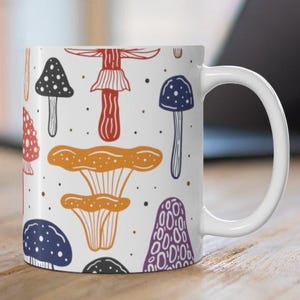White ceramic mug featuring colorful illustrations of various mushrooms, perfect for mushroom enthusiasts and those who love nature-inspired designs.