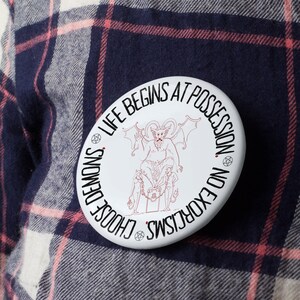 May include: White button with a black and red illustration of a demon with wings and the text "Life Begins At Possession, Choose Demons, No Exorcisms".