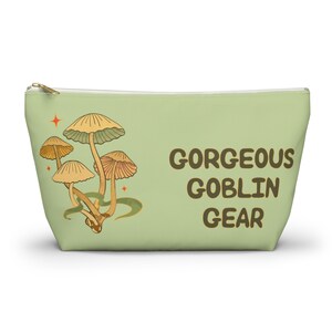 T-bottom pouch in moss green with a mushroom and the words Gorgeous Goblin Gear on the front and a cute snail with a positive message of You're doing great! on the back. Black zipper