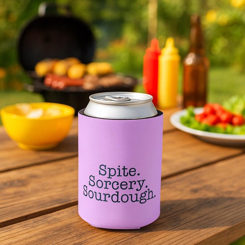 Can cooler featuring a dark serif font design that reads “Spite. Sorcery. Sourdough.” printed on a purple background.