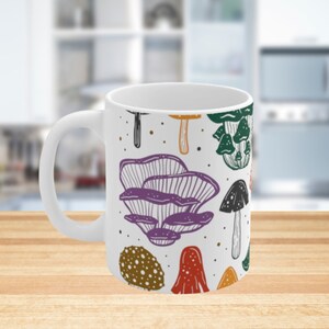 White ceramic mug featuring colorful illustrations of various mushrooms, perfect for mushroom enthusiasts and those who love nature-inspired designs.