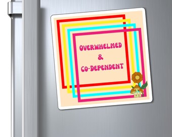 May include: A square magnet with the words "OVERWHELMED & CO-DEPENDENT" in pink text, framed by colourful lines. A flower and mushroom graphic is in the bottom right corner. The magnet is attached to a silver fridge door.