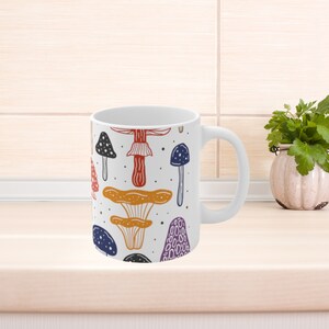 White ceramic mug featuring colorful illustrations of various mushrooms, perfect for mushroom enthusiasts and those who love nature-inspired designs.