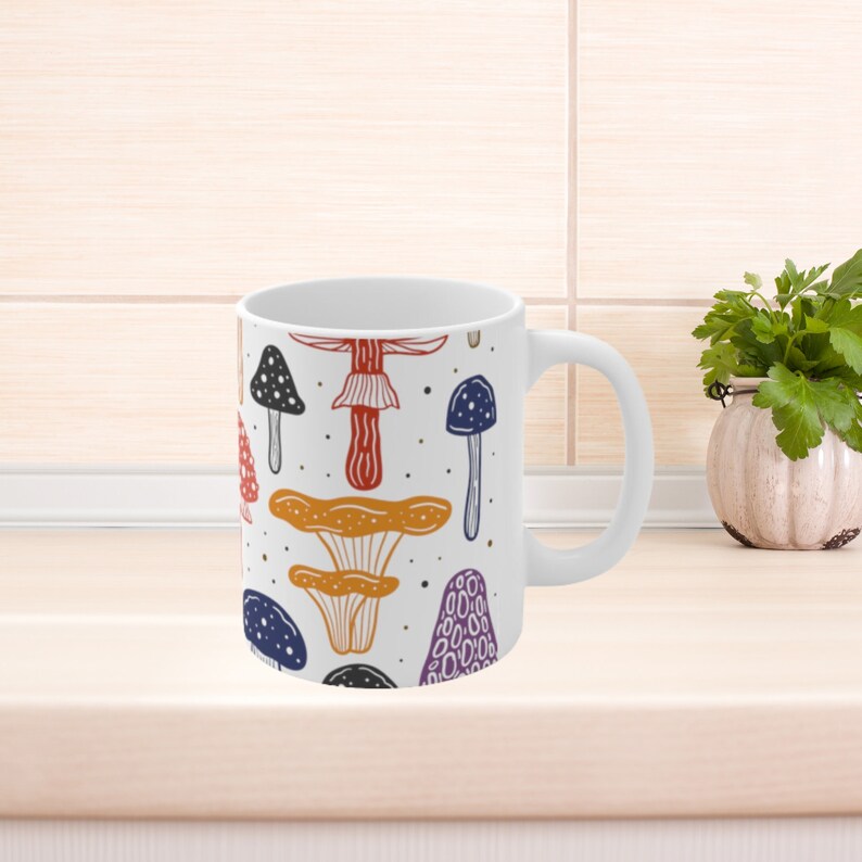 White ceramic mug featuring colorful illustrations of various mushrooms, perfect for mushroom enthusiasts and those who love nature-inspired designs.