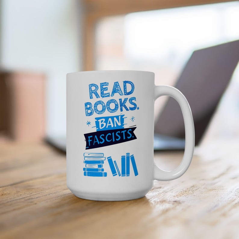 ceramic mug featuring bold blue hand-drawn text that reads "Read Books Ban Fascists" with illustrated books beneath the text.