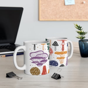 White ceramic mug featuring colorful illustrations of various mushrooms, perfect for mushroom enthusiasts and those who love nature-inspired designs.